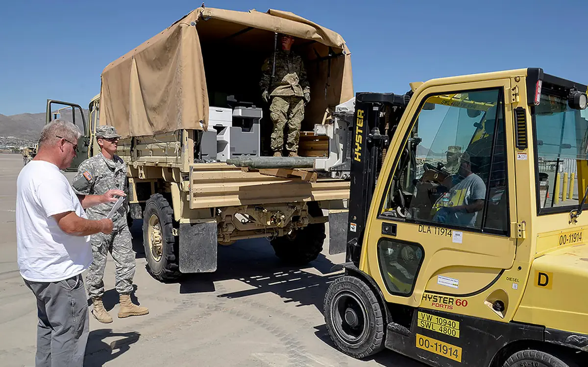 Military cargo truck being loaded by forklift at a defense logistics yard